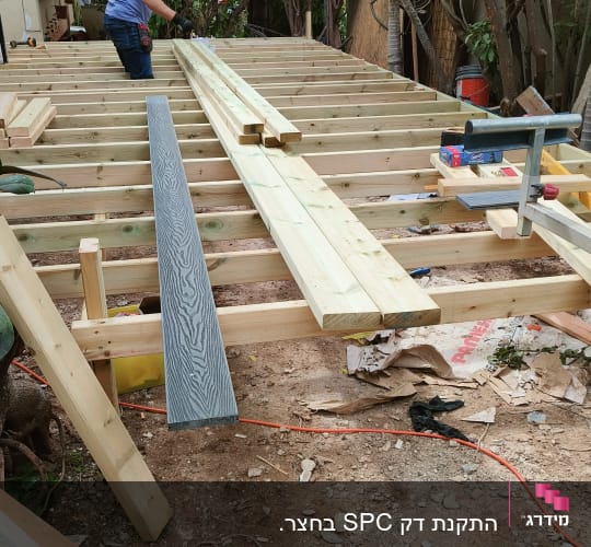 אדם עובד על מבנה עץ בגינה עם עצים מסביב